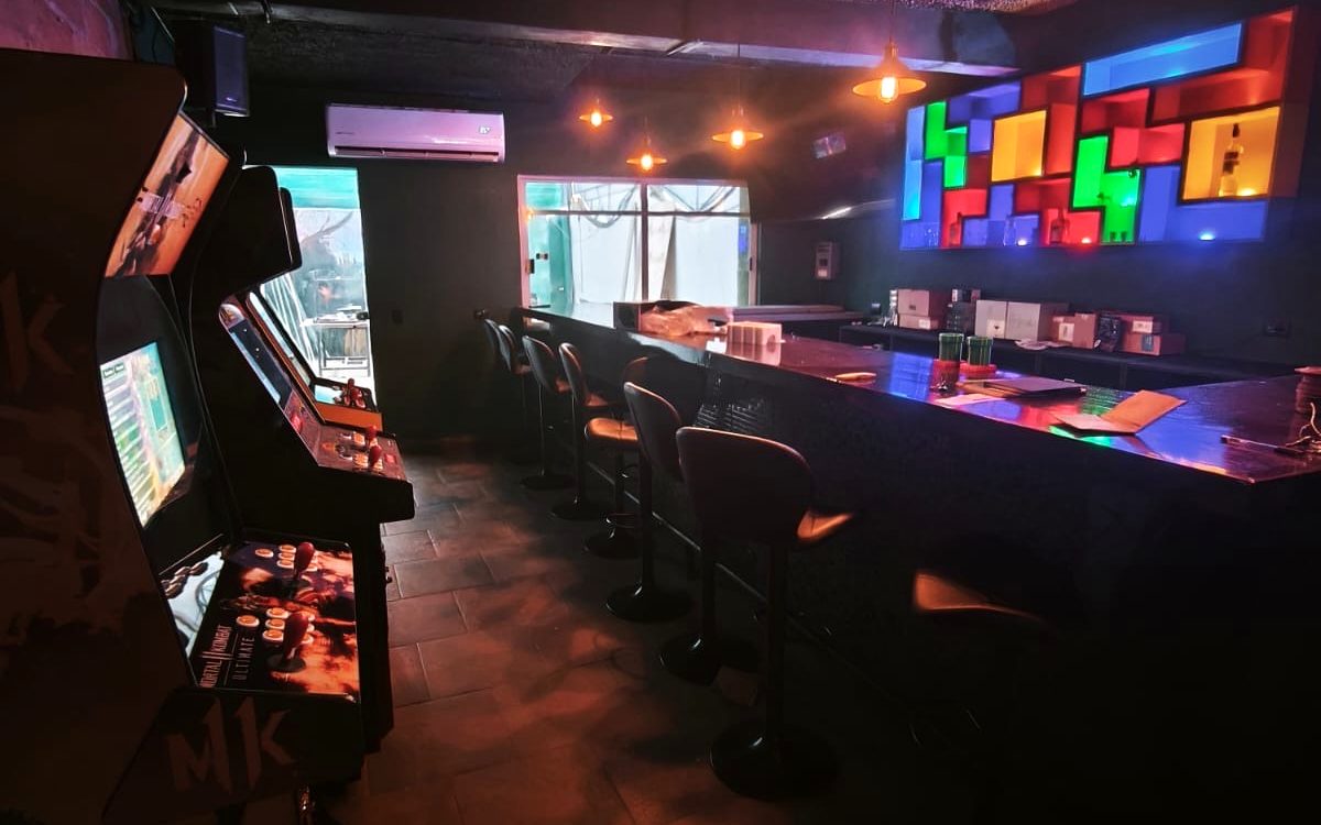 Barra de K.O. con bancos altos, pantallas y la pared de bloques iluminada al fondo